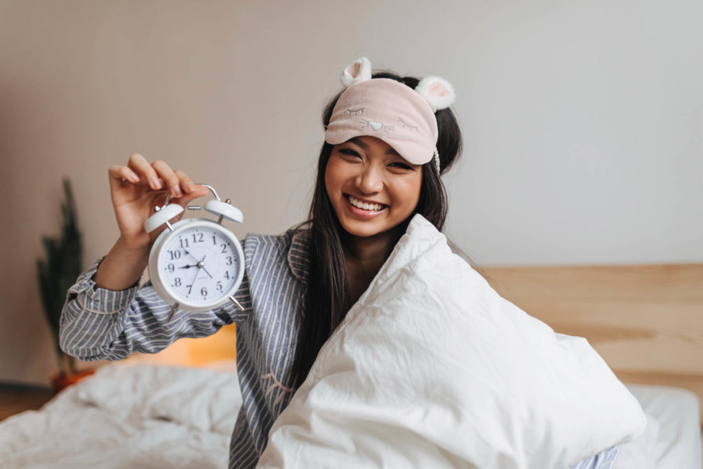 Young girl smiling in bed holding alarm clock