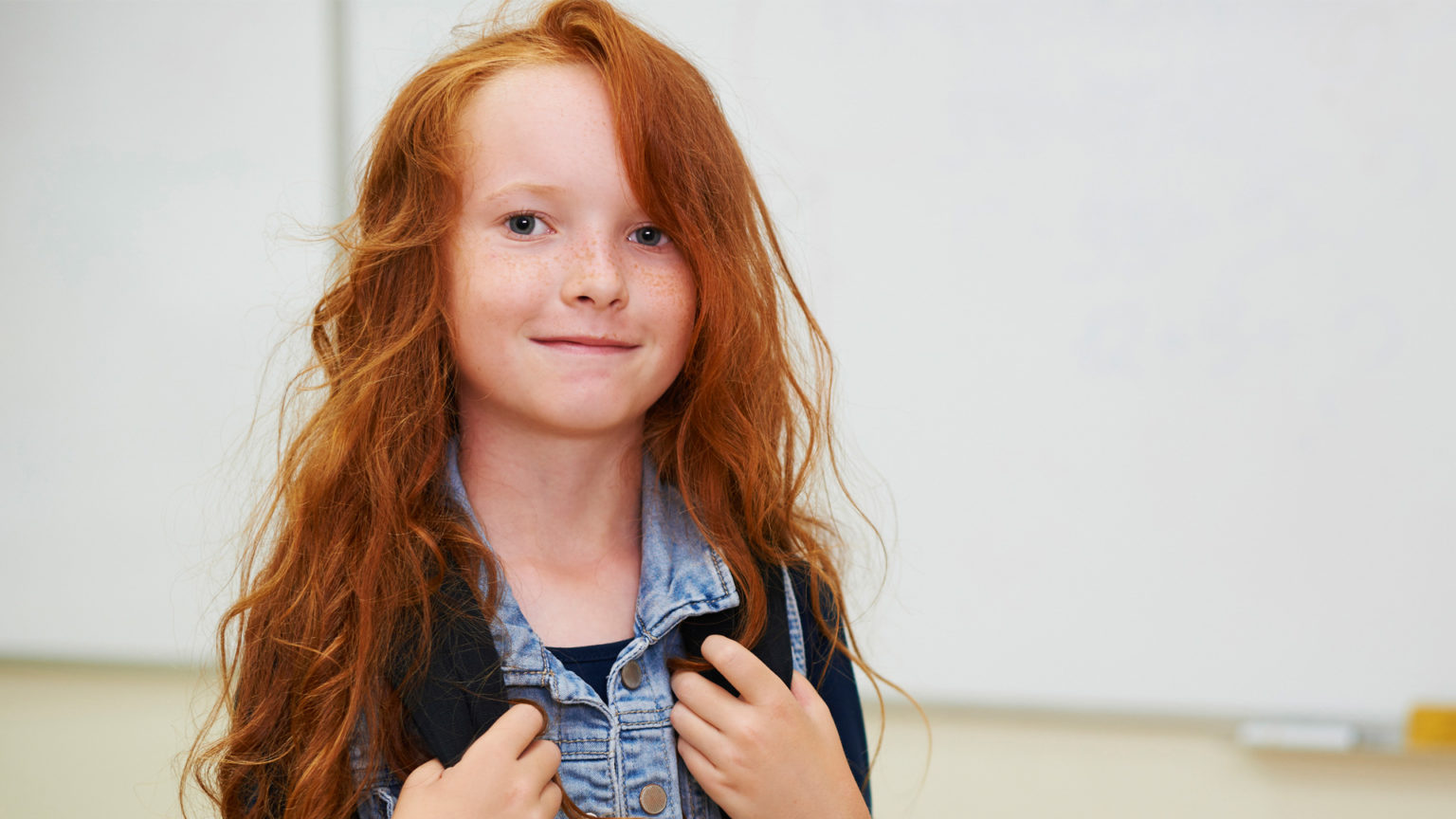 Red head girl going back to school with backpack in the classroom