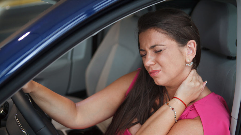 Woman grimacing and holding her neck after an accident and contemplating calling a car accident chiropractor.