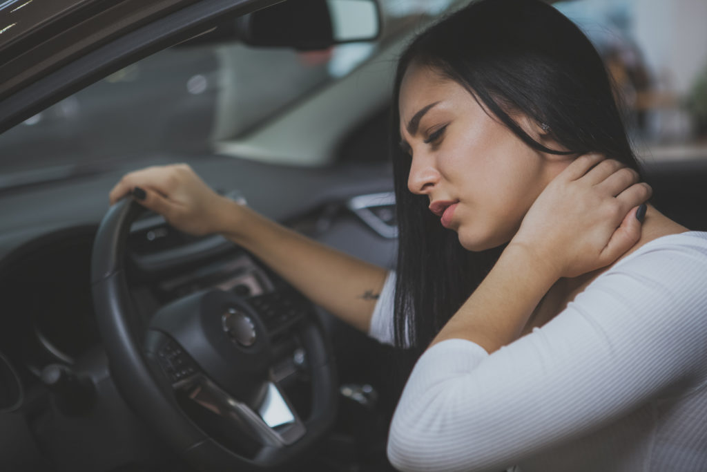 Beautiful young woman rubbing her neck, feeling sore after long drive. Female driver having terrible neck pain after whiplash injury in car crash. Healthcare, safety, pain concept