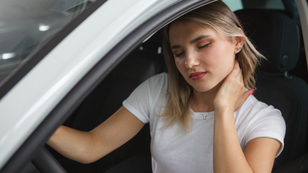 Image of female driver in white shirt grabbing her neck as she experiences one of the common injuries from car accidents.