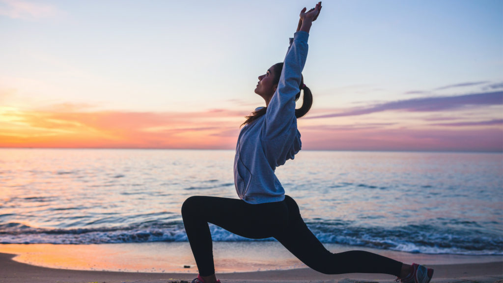 young woman doing sport exercises on sunrise beach in morning, stretching, healthy lifestyle, yoga after boosting her immune system with chiropractic care.
